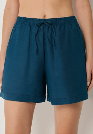 Frau trägt dunkelgrüne Shorts mit elastischem Bund und Kordelzug sowie umgeschlagenem Saum, Hände locker an den Seiten.