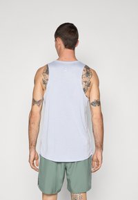 Hellgraues ärmelloses Tanktop mit rundem Ausschnitt und drei vertikalen Akzenten auf der Rückseite, kombiniert mit grünen Shorts. Glatte Stofftextur.