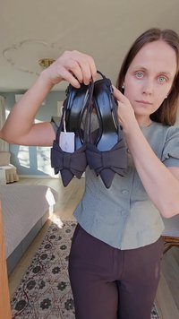 Musta nahkainen korkokengät, joissa on terävät kärjet ja suuret rusetit edessä, minimalistinen muotoilu. Kengän koko on näkyvissä.