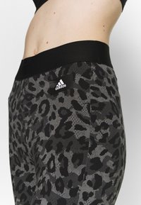 Leggings a vita alta in stampa leopardata nera e grigia con vita nera e una patch del logo Adidas sul lato. Tessuto elasticizzato.