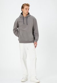 Gray hooded sweatshirt with a front pocket, drawstring, and ribbed cuffs, paired with white cargo pants and white sneakers.