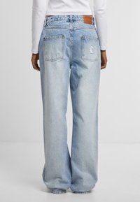 Jeans evazate, de talie înaltă, de culoare albastru deschis, cu un design clasic cu cinci buzunare și o etichetă din piele maro pe banda de la talie.