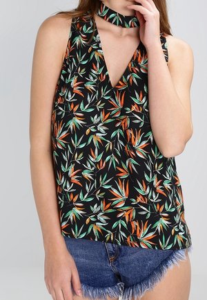 Haut noir sans manches à col halter avec motifs de feuilles orange et vert, porté avec un short en jean bleu effiloché.