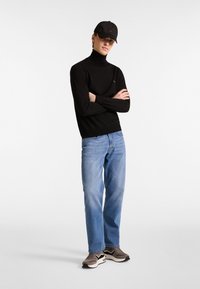 Schwarzer Rollkragenpullover, hellblaue Jeans und braune Sneakers. Die Mütze ist schwarz mit einem Logo. Das Outfit kombiniert schicke und lässige Elemente.