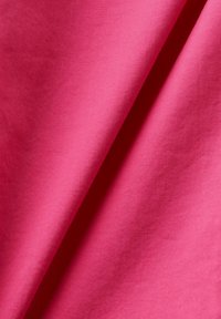 Tissu rose vif et lisse avec des plis doux et une texture de tissage visible sous un éclairage diffus.