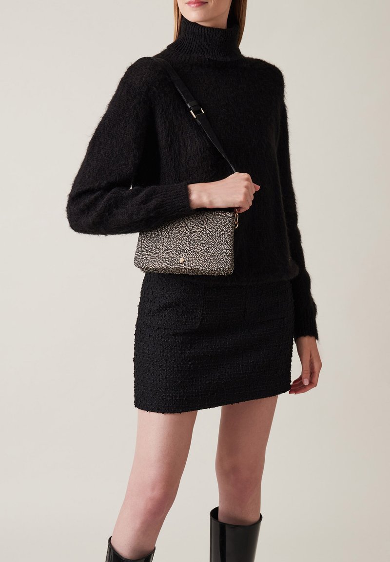 Maglione nero lavorato a maglia, gonna mini nera aderente e borsa a tracolla nera e bianca a trama con un accento dorato. Stivali neri fino al ginocchio.