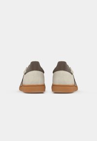 Sneakers in suede grigio chiaro con un tallone in pelle marrone e suola in gomma, caratterizzati da un design semplice e a profilo basso.