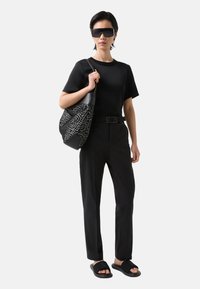 Zwarte T-shirt, op maat gemaakte zwarte broek en zwarte slidesandalen. Grote zwart-wit gestreepte schoudertas. Overmaatse zwarte zonnebril.