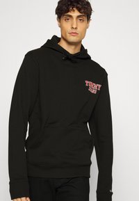 Sudadera negra confeccionada en una mezcla de algodón, que cuenta con un bolsillo frontal, capucha con cordón y un logo rojo de "TOMMY JEANS" en el pecho.