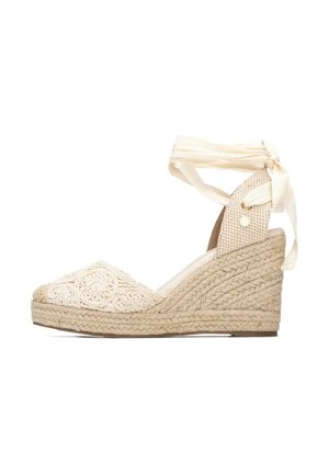 Espadrille cuña beige con suela texturizada tejida, punta cerrada bordada y lazos crema para atar alrededor del tobillo en forma de lazo.
