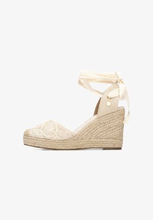 Espadrille cuña beige con suela texturizada tejida, punta cerrada bordada y lazos crema para atar alrededor del tobillo en forma de lazo.
