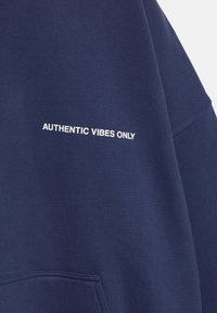 Marineblauwe sweatshirt van zacht katoen met een losse pasvorm; voorzien van witte tekst "AUTHENTIC VIBES ONLY" aan de voorkant.