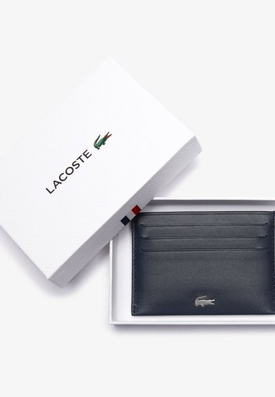 Porte-cartes en cuir marine avec six emplacements, arborant un logo embossé. Présenté dans une boîte blanche texturée, agrémentée de détails rouges et bleus.