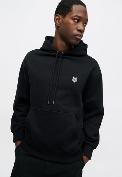 Hoodie noir en tissu doux avec une poche kangourou à l'avant, des cordons de serrage et une petite broderie de loup gris sur la poitrine.