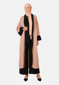 Lang, let robe i blød beige med sorte accenter, der har brede ærmer og et flydende design. Sammen med et sort sæt tøj.