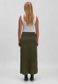 Langer, olivgrüner Rock aus strukturiertem Stoff, mit tailliertem Bund und geradem Schnitt, kombiniert mit schwarzen High-Heel-Stiefeln.