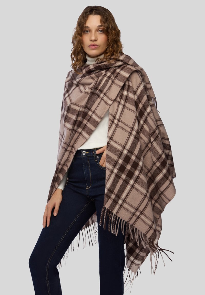 Brązowy i beżowy koc w kratę z frędzlami, wykonany z miękkiego materiału. Noszony na białym swetrze i ciemnych dżinsach.