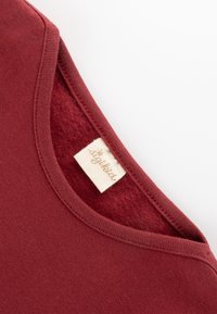 Burgunder Baumwoll-T-Shirt mit Rundhalsausschnitt und weicher Innenstruktur. Verfügt über einen genähten Halsausschnitt und ein Etikett mit "sigikid"-Branding.