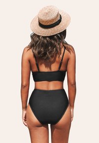 Conjunto de bikini negro con top bandeau y parte inferior de talle alto. Estilizado con un sombrero de paja con una banda negra. Textura suave, diseño minimalista.