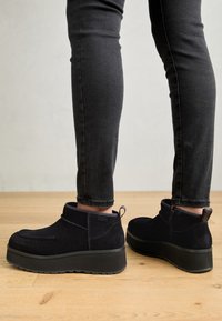 Crne suede gležnjače s okruglim vrhom, s masivnom platformom i zatvaranjem na cipelu. Teksturirani detalji na peti.