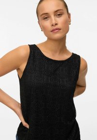 Czarny bezrękawnik o teksturowanym wzorze koronkowym, z okrągłym dekoltem i lekko luźnym krojem. Udekorowany skomplikowanymi wzorami geometrycznymi.