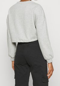 Felpa corta grigia con maniche ampie; texture morbida; orlo a costine. Abbinata a pantaloni cargo neri con tasche laterali e vita aderente.