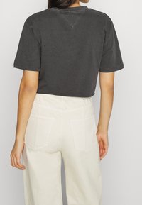 Šedé zkrácené tričko s krátkým rukávem, které má kulatý výstřih a minimální švy, v kombinaci s krémovými kalhotami s vysokým pasem.