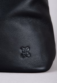 Black leather bag with textured surface, featuring a subtle embossed detail of a bow at the bottom corner. Shape is soft and rounded.