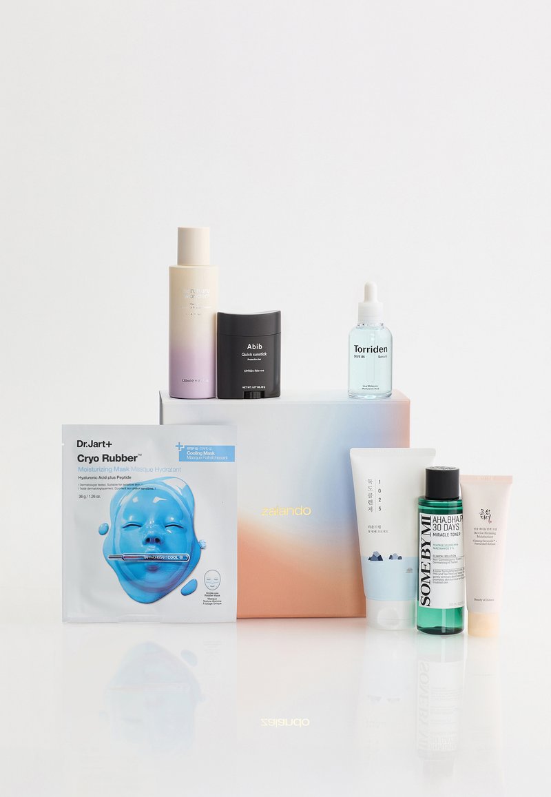 Huidverzorgingsset met zeven producten, waaronder een hydraterend masker, toner, serum, zonstick en crème, weergegeven op en rond een Zalando-doos.