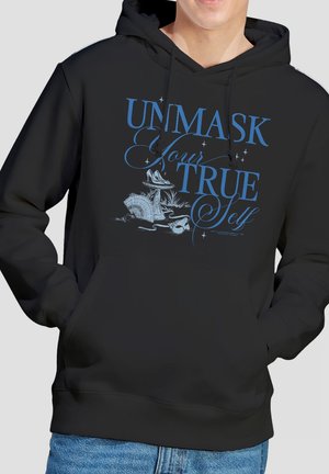 Person trägt schwarzen Hoodie mit blauem Schriftzug "Enthülle dein wahres Ich" und Illustration einer Vintage-Maske, eines Fächers und Schuhe auf der Vorderseite.