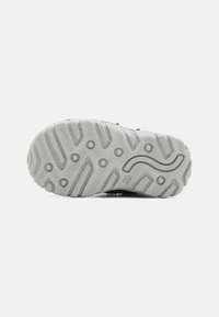 Suela de goma gris con un patrón texturizado, que presenta agarraderas circulares y un diseño de acento ondulado. La parte inferior es ligeramente curva para mayor flexibilidad.
