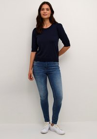 Haut à manches courtes bleu marine en tissu doux, associé à un jean bleu ajusté et des baskets blanches, présentant une tenue décontractée au design simple.