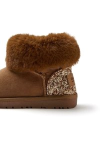 Botín marrón hasta el tobillo con cuello de piel sintética, material de ante, panel texturizado de purpurina en el costado y una suela de goma con pequeños patrones de relieve.