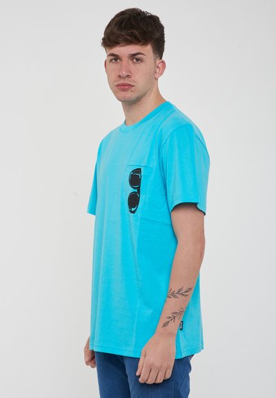 T-shirt turchese a maniche corte con tasca, caratterizzato da una grafica di occhiali da sole neri. Tessuto morbido, vestibilità comoda e dettagli con scollatura rotonda.