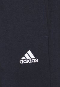 Pantalones de chándal de color navy hechos de tela suave, con el logo blanco de Adidas en el lado izquierdo. El diseño incluye bolsillos y una textura suave.