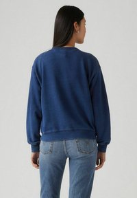 Marinblå sweatshirt med rundad halsringning och ribbade muddar, kombinerad med ljusblå denim jeans. Slät struktur, avslappnad passform, minimalistisk design.