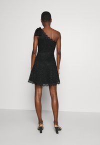 Svart spetsklänning med en axel och en rosett, utsvängd kjol och spetsdetalj vid fållen. Slät textur och figursydd midja.