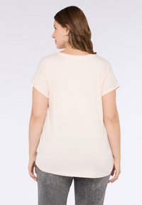 Top scurt bej deschis cu guler rotund, croială lejeră și accente cu slit pe laterale, asociat cu pantaloni gri texturat.