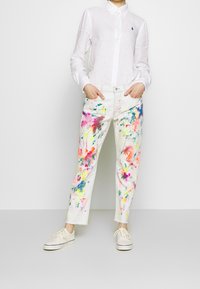 Bílá bavlněná košile na dlouhý rukáv s knoflíky. Barevný design fleků na bílých denimových kalhotách. Volnočasové boty se šněrováním. Zkrácený lem na kalhotách.