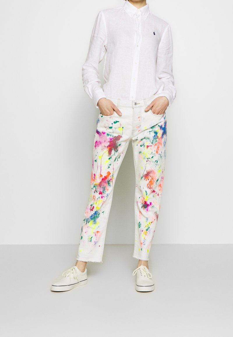 Bílá bavlněná košile na dlouhý rukáv s knoflíky. Barevný design fleků na bílých denimových kalhotách. Volnočasové boty se šněrováním. Zkrácený lem na kalhotách.