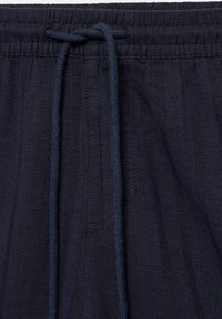 Pantalon de survêtement en tissu bleu marine avec ceinture élastique et cordon noué au centre devant.