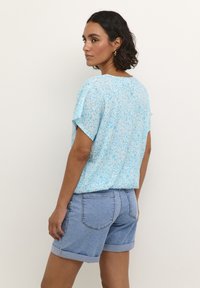 Top corta a maniche corte blu chiaro con motivo floreale e vestibilità rilassata, abbinato a pantaloni corti in denim con risvolto. Entrambi i capi presentano una texture morbida e un design casual.