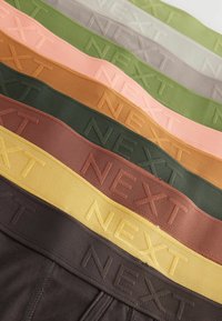 Zeven stoffen taillebanden in verschillende kleuren, elk voorzien van de opdruk "NEXT," met gladde texturen en verschillende tinten zoals groen, bruin en perzik.