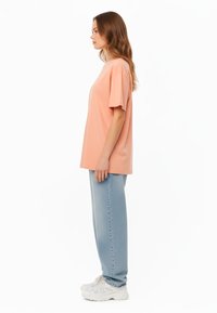 T-shirt oversize a maniche corte in tessuto pesca chiaro, abbinata a jeans larghi di colore blu chiaro e sneakers bianche chunky.