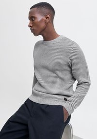 Pull gris côtelé à manches longues, avec un col rond et un tissu texturé. Détail de couture notable et petite étiquette de marque à l'ourlet.