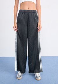 Black pinstriped wide-leg pants with an elastic waistband, featuring white side stripes and an adidas logo on the left thigh. Soft texture.
