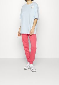 Světle modré volné tričko s nášivkou loga, v kombinaci s růžovými tepláky. Obuv tvoří bílé vysoké tenisky.