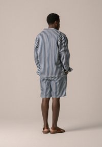Completo di cotone a righe composto da una camicia a maniche lunghe e pantaloni corti in blu e bianco. Include un colletto a polo e una vestibilità comoda. I sandali sono marroni.