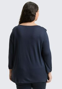 Navy blauwe shirt met lange mouwen en een ronde hals, zachte textuur en zijsplitten aan de zoom, gezien vanaf de achterkant.