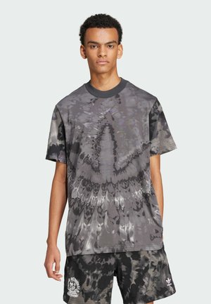 Siva majica od pamuka s tie-dye uzorkom, opuštenog kroja, okruglog izreza i izraženim zavojitim uzorcima. Uparena s kratkim hlačama s odgovarajućim uzorkom.